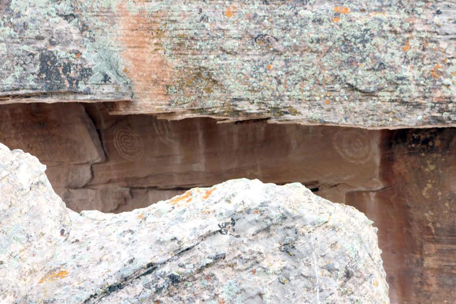 A row of three petroglyphs have been pecked on the smooth, nearly vertical face underneath the overhanging ledge of the larger boulder