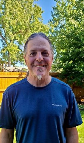 Pat wearing a bright blue t-shirt, standing outdoors, and smiling