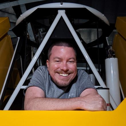 Head shot of Damon smiling and looking out from a telescope structure