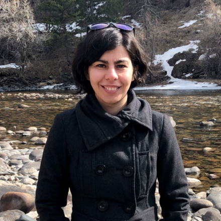 Soudeh Kamali in a winter belted coat standing in front of a rocky stream