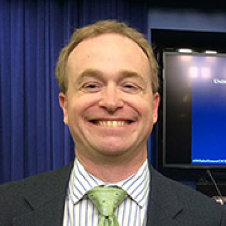 Mike smiling with gray suit and bright green tie